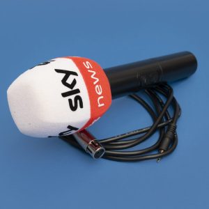 Handheld microphone with a white foam windscreen and an orange band featuring “news” text, shown with a cable on a blue background.